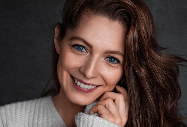 Smiling woman with auburn hair resting her hand near her face