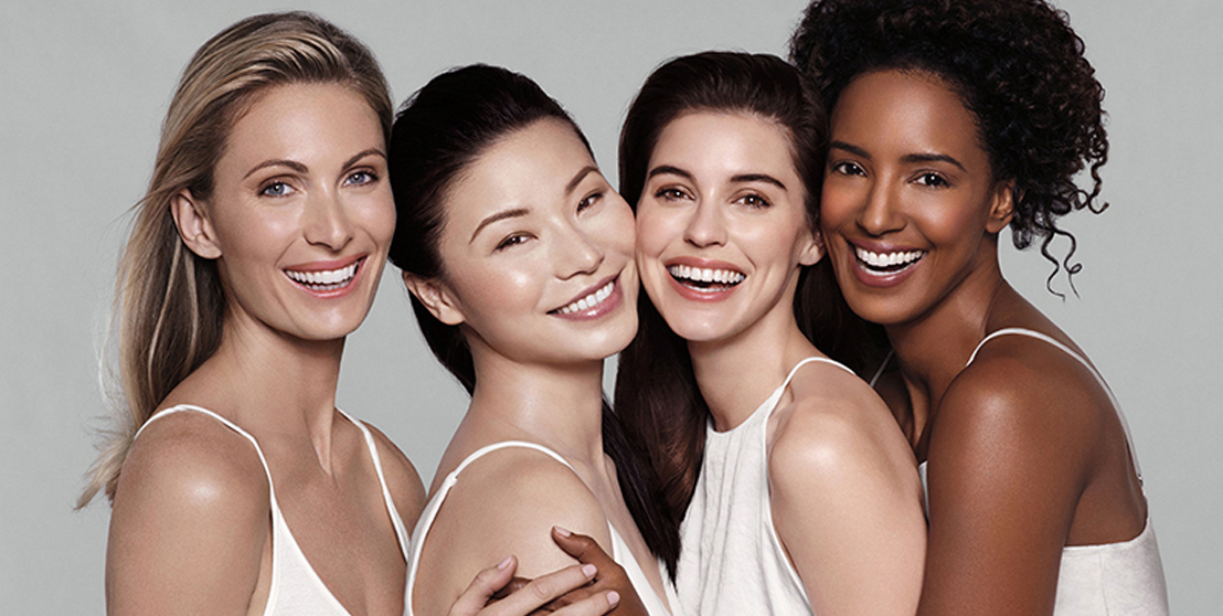Four smiling women in white outfits against a gray background